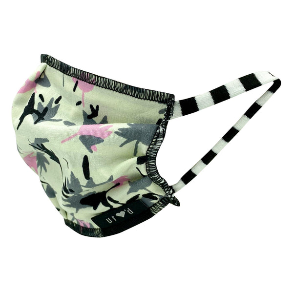 Pleated and lined kids face mask with an abstract print of overlapping grey, pink, and black palm tree-like shapes on a white background, with black and white striped stretch cotton ear loops. Hand-sewn in the USA, sustainably made in eco-conscious fair labor facilities with upcycled materials.