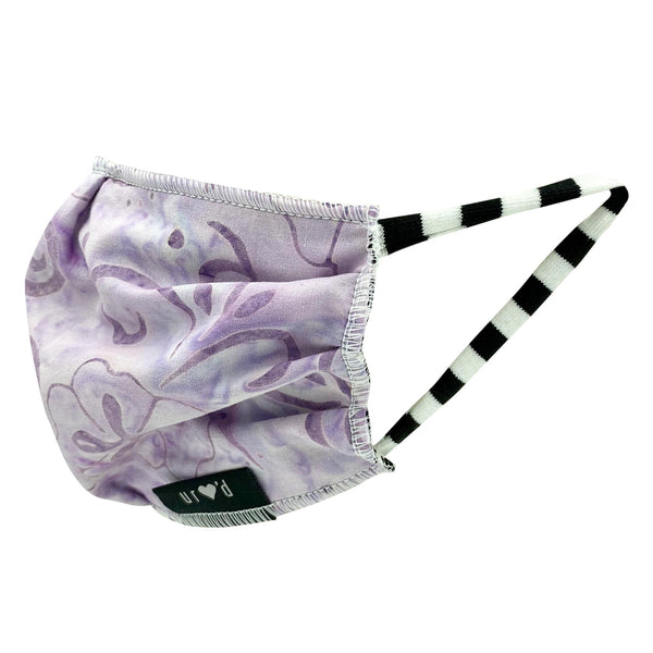 Pleated and lined kids face mask with light purple batik print, with black and white striped stretch cotton ear loops. Hand-sewn in the USA, sustainably made in eco-conscious fair labor facilities with upcycled materials.