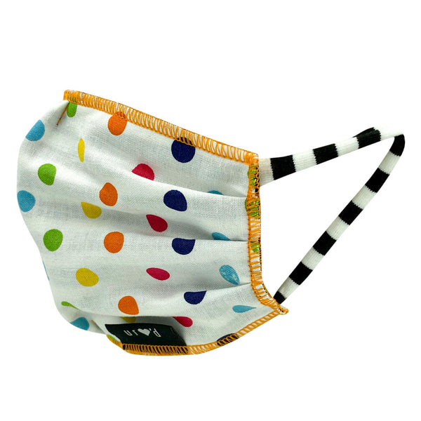 Pleated and lined kids face mask with a print of multicolored dots on a white background, and orange stitching outlining the body of the mask, with black and white striped stretch cotton ear loops. Hand-sewn in the USA, sustainably made in eco-conscious fair labor facilities with upcycled materials.